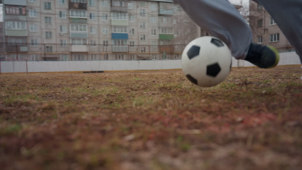 혼자 하는 도시 축구 연습, 텅 빈 도시 환경에서 드리블 기술을 연습하는 외로운 선수, 낮 시간 동안 비어 있는 도시 운동장에서 혼자 제어된 축구 훈련을 수행하는 남자