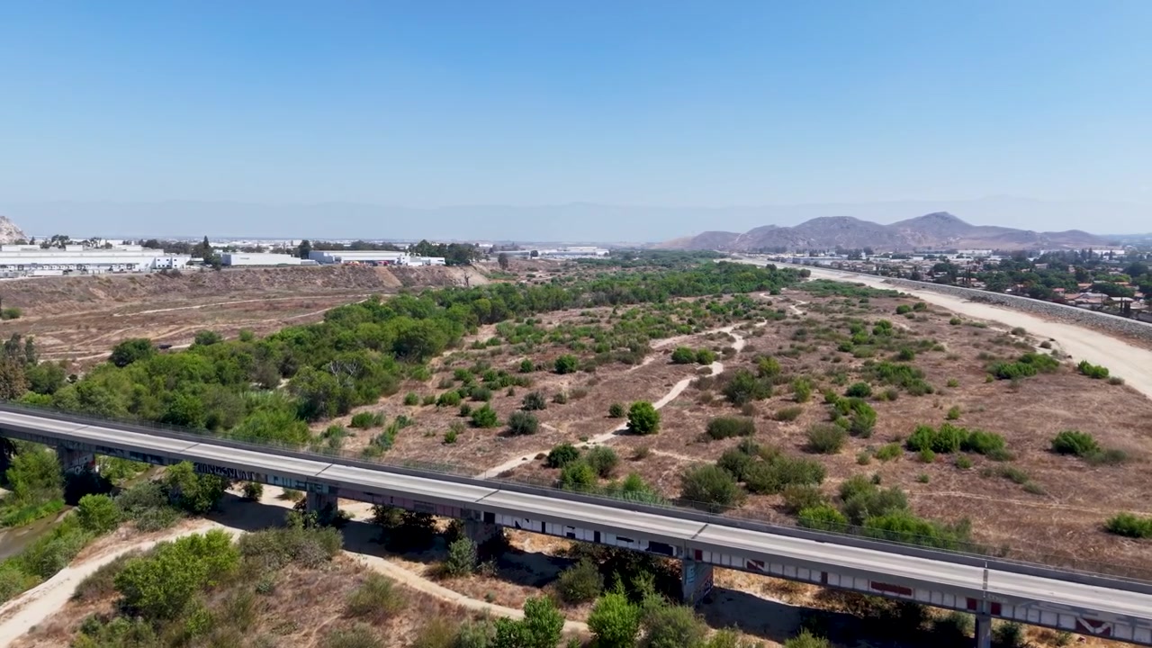 Aerial drone footage above the Santa Ana Riverbed in Riverside California, revealing a graffiti-covered overpass. elevated perspective captures the urban waterway and surrounding landscape.