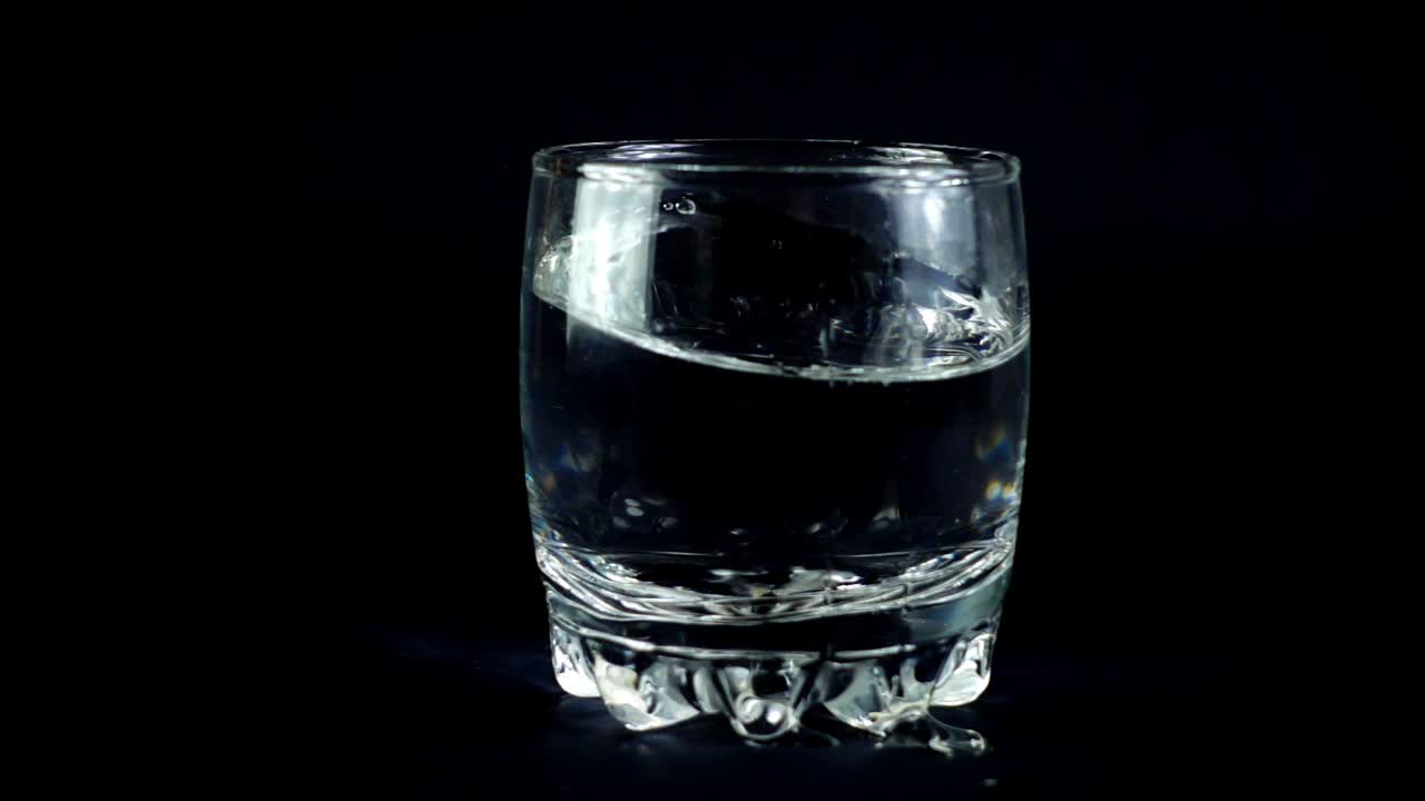 Vand i et glas på en sort baggrund. Slowmotion.