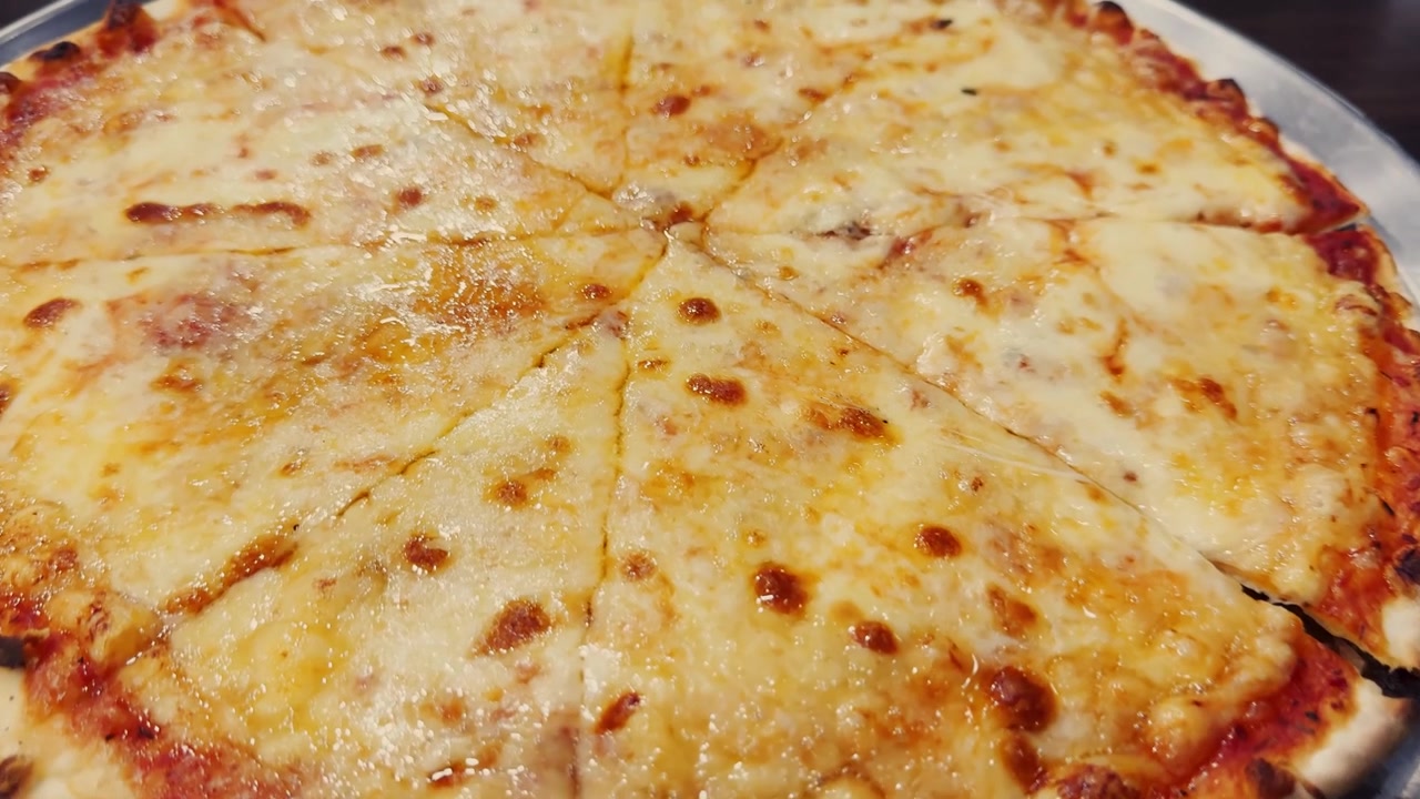 Pizza al formaggio intera su un vassoio di metallo, tagliata a fette con mozzarella fusa, crosta dorata, bordo di salsa di pomodoro e apparecchiatura informale da ristorante.