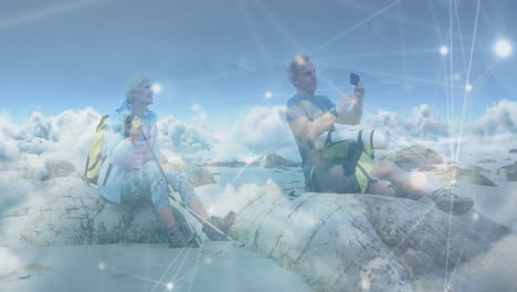 una pareja de ancianos caucásicos haciendo senderismo, tomando fotos con su teléfono inteligente, sobre las nubes y la red de conexiones.