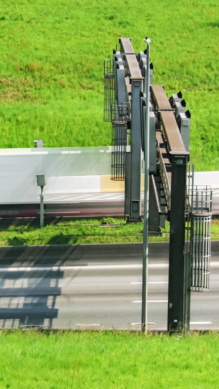 Daytime timelapse of cars and trucks racing past roadside speed cameras beside a bright green embankment