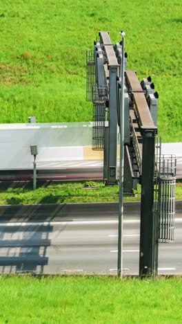 daytime timelapse of cars and trucks racing past roadside speed cameras beside a bright green embankment