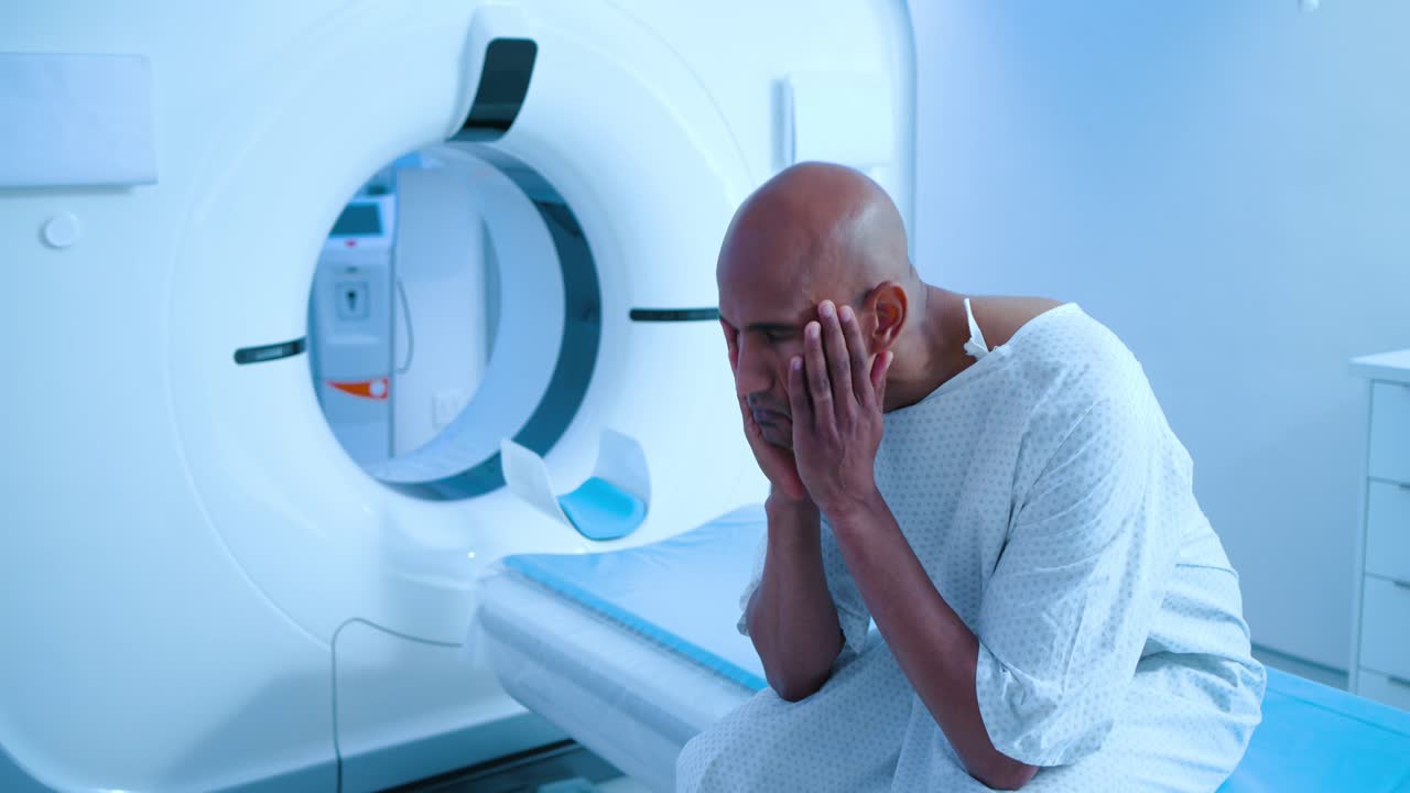 Un paziente di sesso maschile si sta stabilizzando sul lettino dello scanner, si sfrega la mascella e gli occhi mentre aspetta l'inizio della scansione