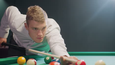 billiard player in white shirt leans over green pool table in dimly lit room, gripping cue stick with focus. dark background enhances intensity as he lines up precise shot in competitive game