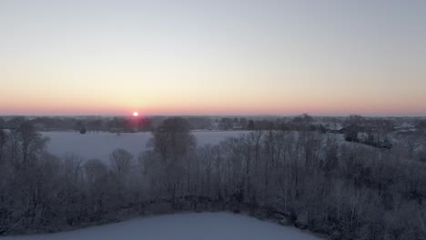 dolly forward over a snowy field and trees towards the sun rising on the horizon.