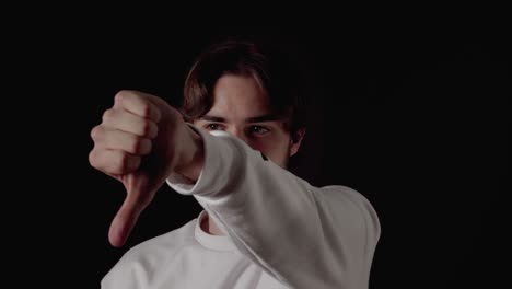 trendy young man giving thumbs down, disapproving gesture, close, black background