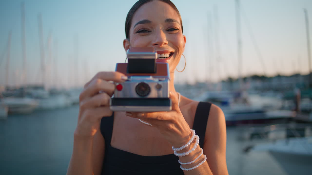 mujer feliz tomando una foto polaroid en la marina al atardecer