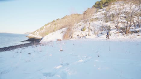 Distant-Man-With-Backpack-Trek-With-His-Dog-Pet-On-Snowy-Mountains-By-The-Lakeshore