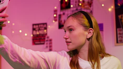 young woman taking a selfie with her phone in her bedroom