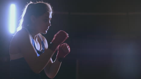 training a beautiful female boxer doing punches in a dark room. steadicam shot. preparation for self-defense and fight in the ring