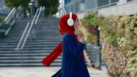 young woman in hijab listening to music and dancing outdoors