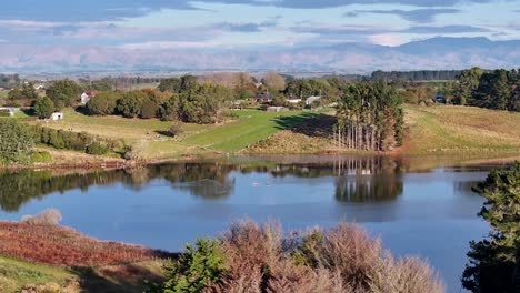 Drone-fly-over-calm-lake-with-reflection,-New-Zealand-rural-countryside