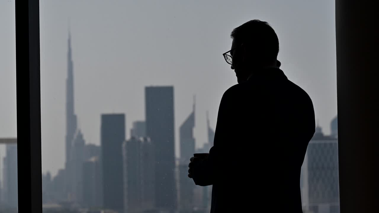 4K: Silhouette of a businessman talking over the phone by the window, The World's tallest building 'Burj Khalifa' in the background
