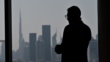 4k:-Silueta-De-Un-Hombre-De-Negocios-Hablando-Por-Teléfono-Junto-A-La-Ventana,-El-Edificio-Más-Alto-Del-Mundo-&#39;burj-Khalifa&#39;-En-El-Fondo