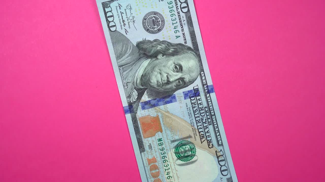 Cento dollari in rapida rotazione su uno sfondo rosa girevole