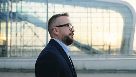 Side-View-On-The-Handsome-Businessman-In-Glasses-Walking-Outdoor-Big-Glass-Urban-Building-Of-Airport