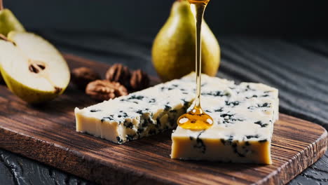 honey being drizzled over blue cheese with pear and walnuts on a wooden board