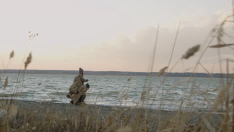 Fear-View-Of-Two-Friends-In-Winter-Clothes-Throwing-Pebbles-To-The-Water-On-A-Seashore-On-A-Cloudy-Day