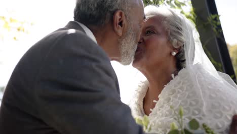 happy senior biracial couple kissing during wedding ceremony in garden, slow motion