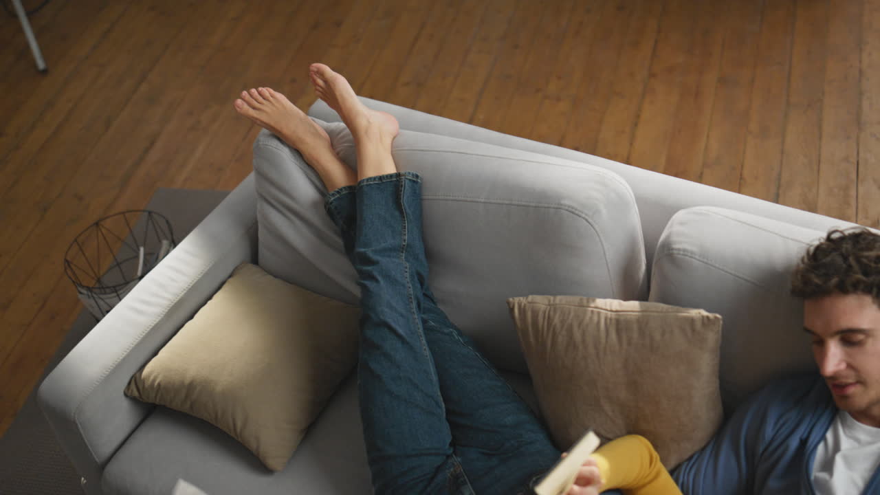 Calm sweethearts reading novel at grey sofa closeup. Romantic man caressing wife