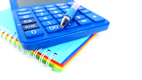 blue calculator, pen, and rainbow notebook