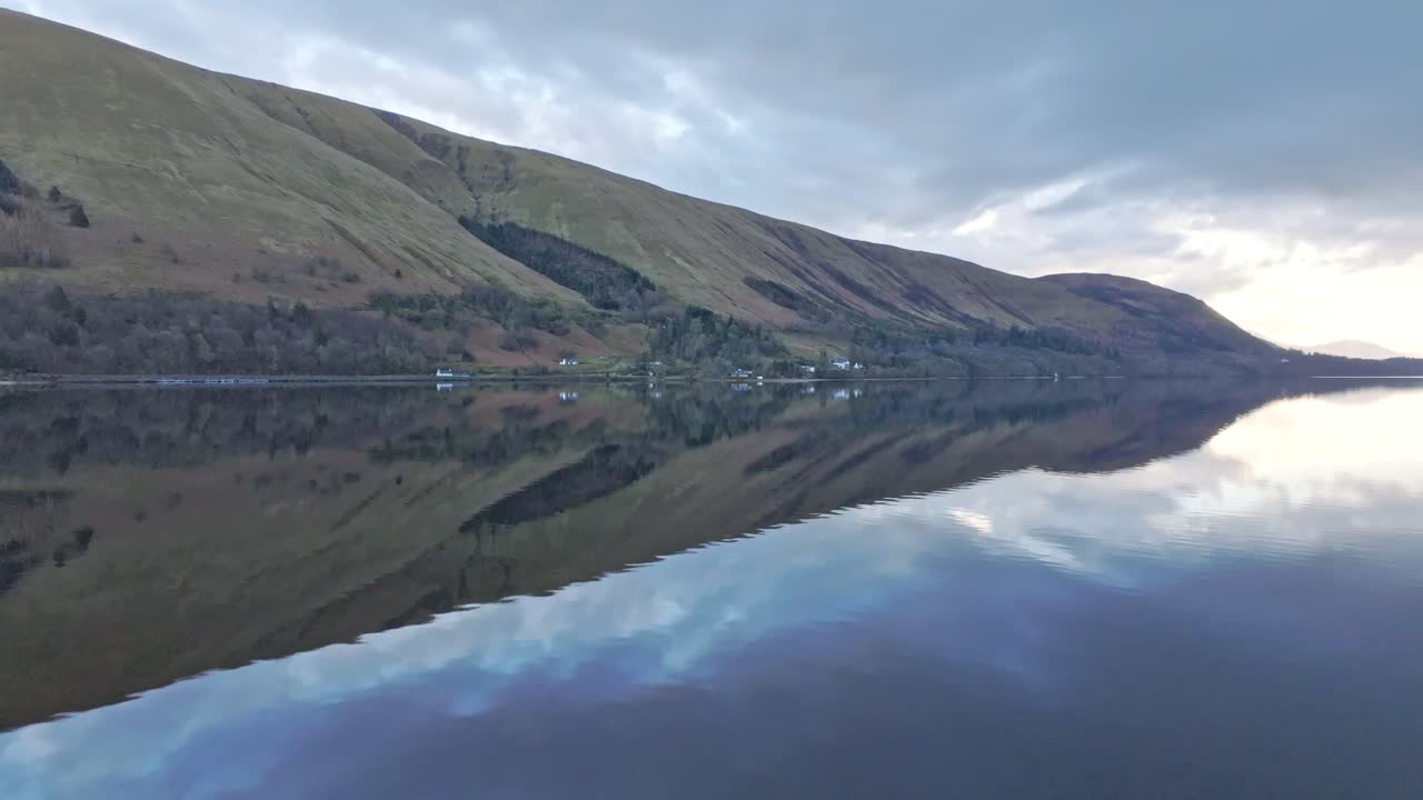 Cinematic aerial drone shot of a solitary lake (Scottish loch) surrounded by mountains and forest