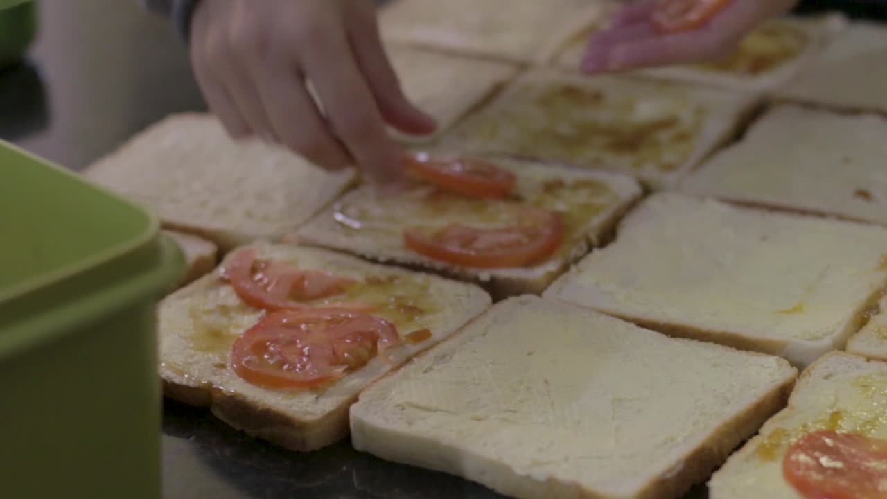 mujer joven poniendo rodajas de tomate en un sándwich para asar para el almuerzo