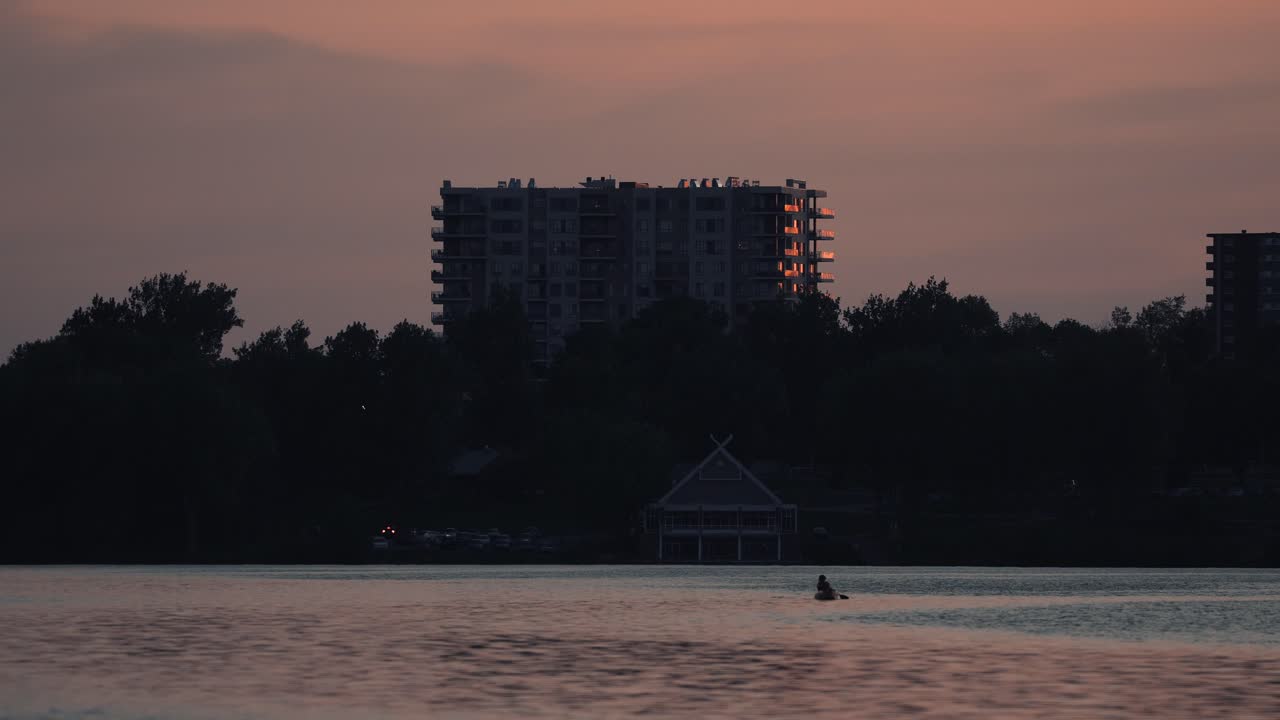 glorioso paisaje de puesta de sol en el lago de las naciones en sherbrooke, quebec, canadá con una persona remando en un bote y un edificio moderno en el fondo - plano general