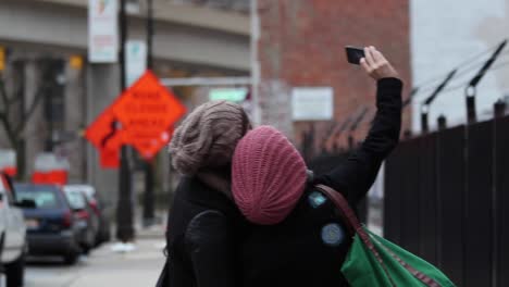 two friends take a selfie in the streets of detroit, they have their back to the camera and then turn around