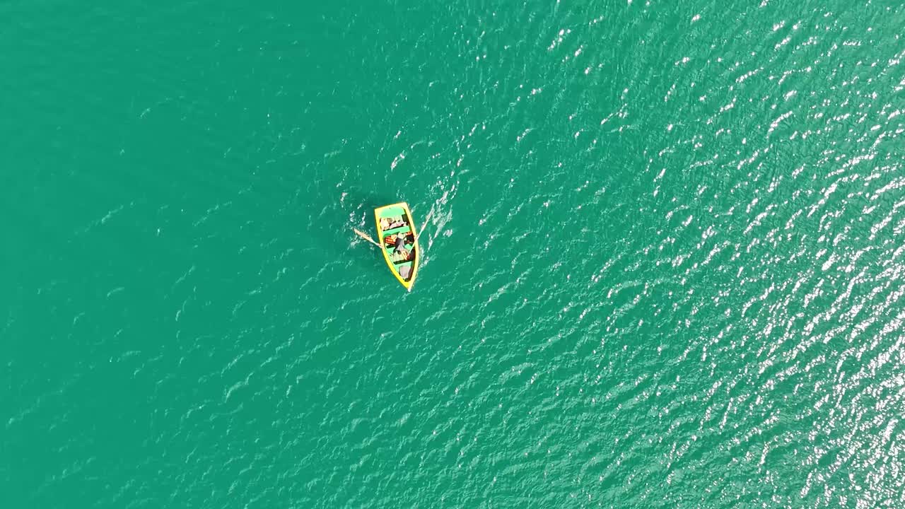 Top-down aerial view of Lake Rocotuyoc near Huaraz, Peru, showing turquoise water and a man rowing a yellow boat under bright sunlight in a peaceful mountain setting