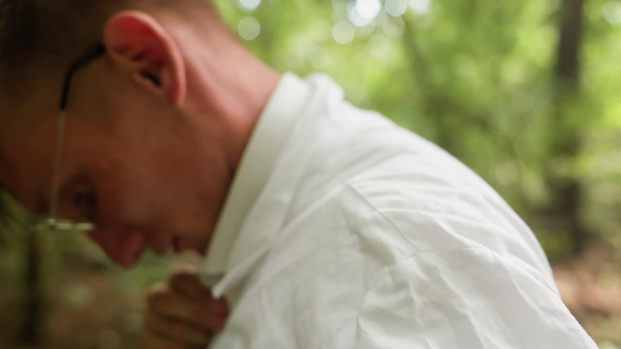 Close view of botany student in white shirt adjusting coat in blurred forest, surrounded by natural greenery, highlighting outdoor lifestyle, preparation, focus, and activity within woodland