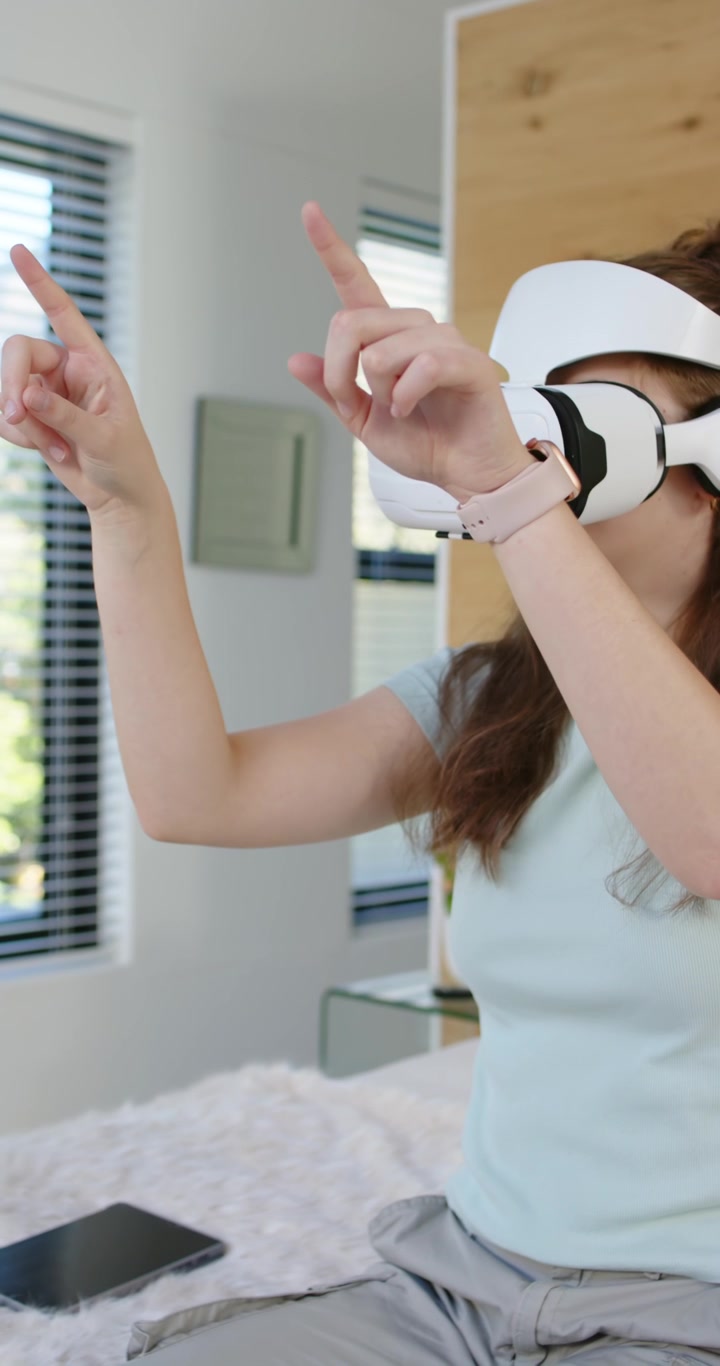 Video verticale: Donna adulta che indossa un visore VR, che indica, pizzica e trascina l'interfaccia utente a letto con un tablet.
