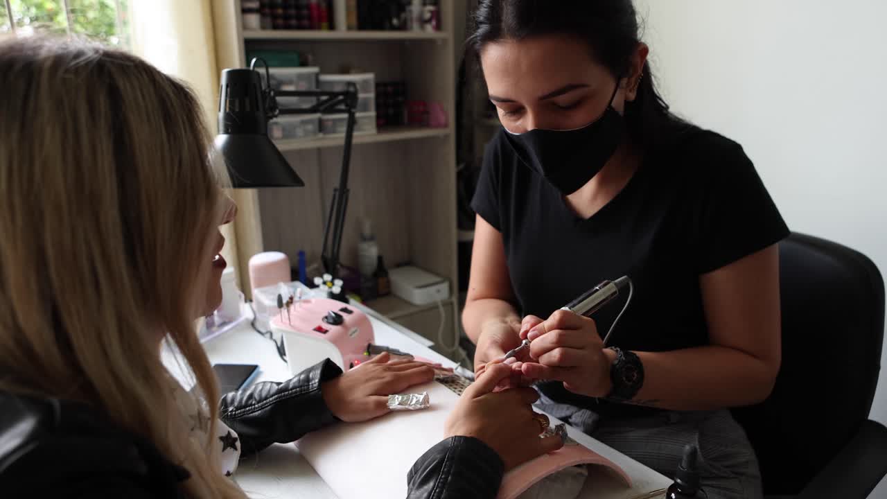 maestra usando papel de aluminio mientras hace manicura para el cliente en el salón