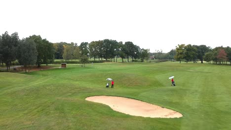 a drone lowers down to the ground pulling two golfers into view playing in the rain