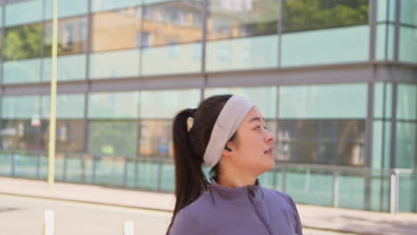 Close-Up-Side-View-Of-Young-Woman-Exercising-Running-Along-City-Street-Wearing-Wireless-Earbuds-Resting