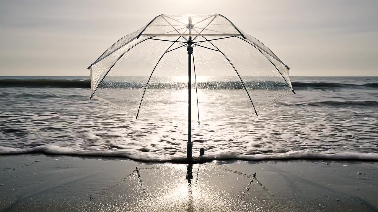Gennemsigtig paraply på en strand under en fredfyldt gylden solnedgang