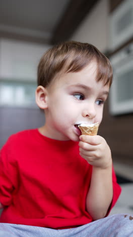 Charming Caucasian toddler eating an ice-cream on the waffle cone. Happy sweet tooth kid portrait. Close up. Vertical video.