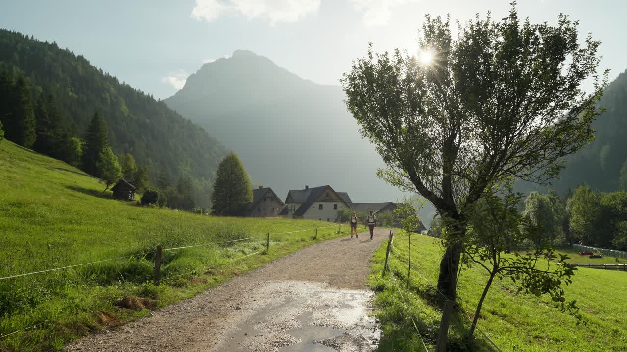 A peaceful valley scene with hikers walking a dirt path through lush green hills in Slovenia