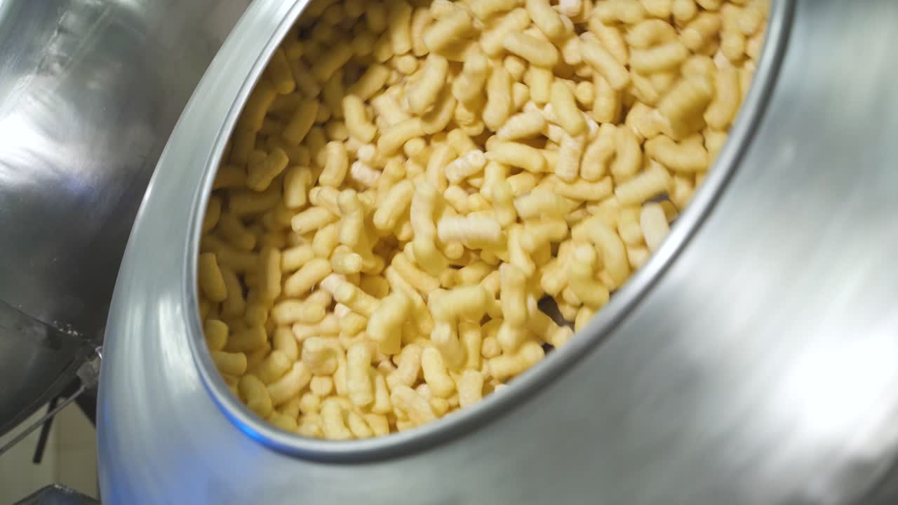 Rotating metal container with crispy corn sticks snacks. Tank for mixing products in a food factory