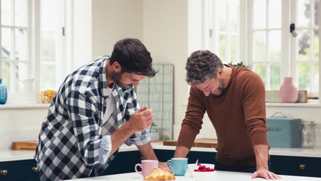 same sex male couple at home in kitchen having breakfast together