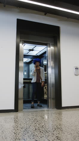Vertical video of biracial businesswoman talking on smartphone and using elevator, slow motion