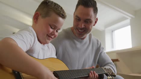 smiling caucasian father with son playing guitar together and sitting in living room