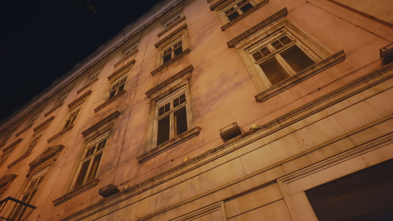 Vista dal basso di una vecchia facciata di edificio di notte con ombre di alberi in movimento