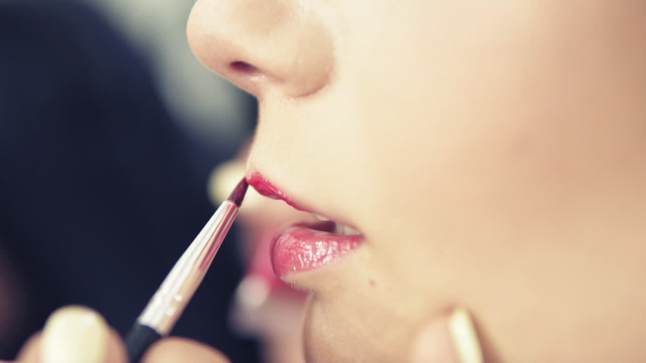 el maquillador pinta los labios de una chica hermosa usando un pincel de lápiz labial. modelo con lápiz labial. lápiz labial rosa en los labios. tonos de moda de