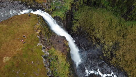 stunning 4k aerial of a large waterfall flowing down moss covered mountain