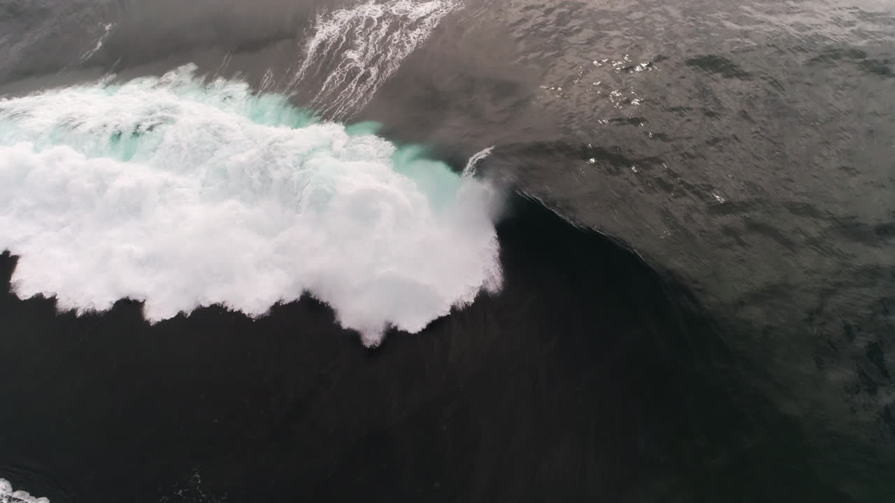 Slow motion wave folds in half with glowing crest under soft evening sky