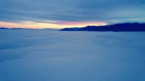 Epic-aerial-orbit-of-mountain-sunrise-above-the-clouds,-cloud-cover-with-El-Plomo-Mountain-snow-capped-Andes-Mountain-Range