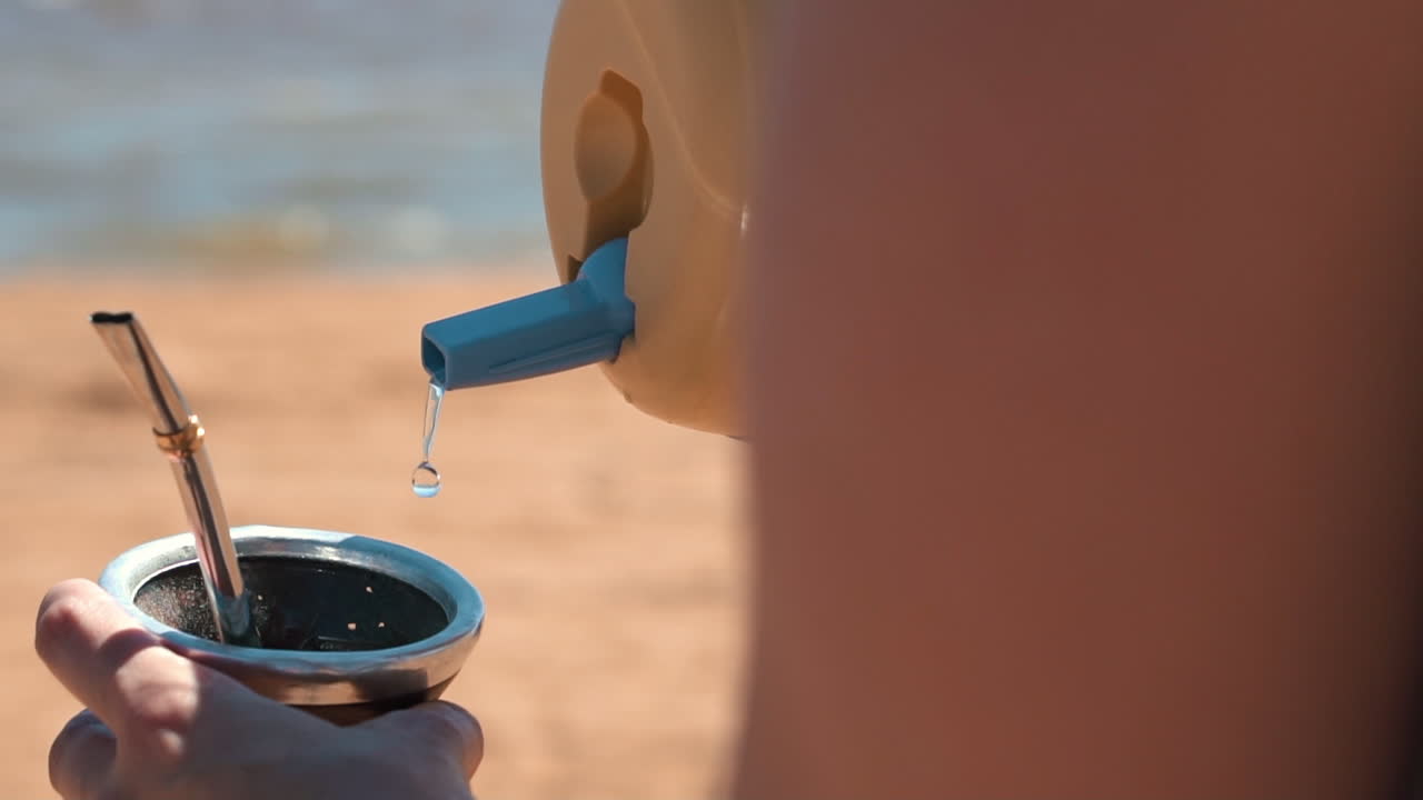 An image depicts the pouring of water into a traditional terer&eacute; gourd, showcasing the cherished ritual of preparing and enjoying this refreshing South American drink