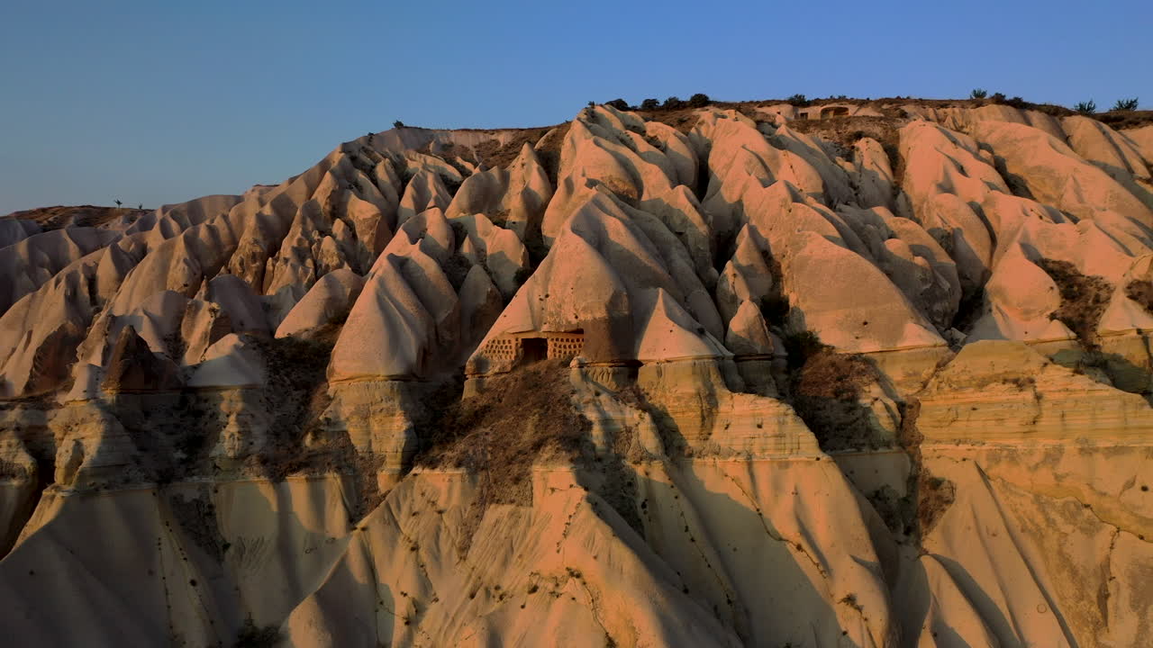 터키 카파도키아에서 주변 산을 드러내기 위해 암면에 새겨진 작은 오두막의 서사시적인 드론 샷